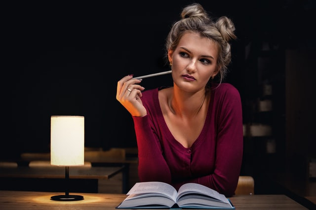 Woman sitting down reading a book and looking pensively to her right side