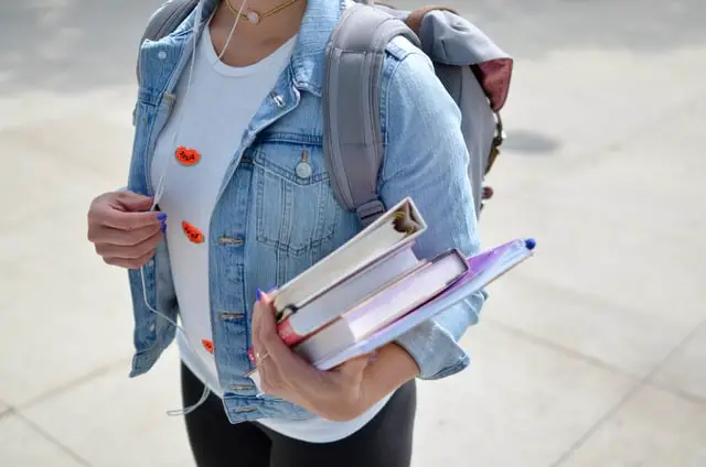 Student holding books and backpack while walking on campus